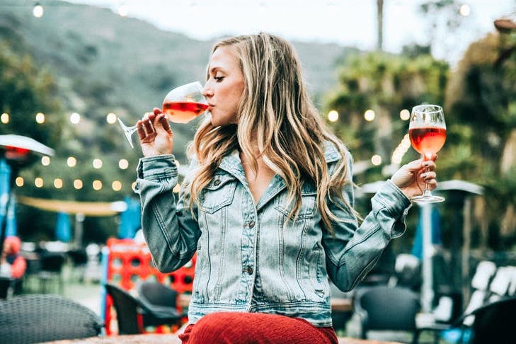 Gilr drinking one glass of wine with another glass of wine in the other hand.